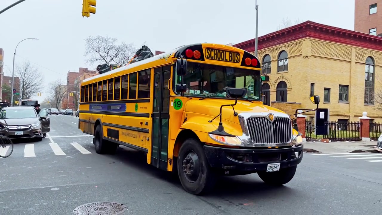 New York, USA, 9 March 2022: Yellow school bus side view on New York street. Side view of yellow school bus with blue stripe, tinted windows, number 19, urban street reflections.