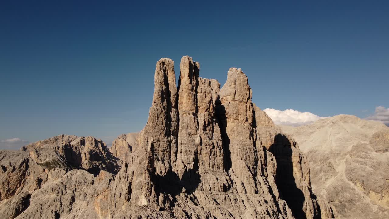 Sharp rugged mountain peak rises dramatically under clear blue sky in Dolomites region of Italy captured from drone showcasing geological textures and alpine wilderness