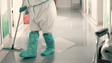 Lower-shot-of-janitor-mopping-hospital-floor-in-covid-19-protective-gown-and-booties