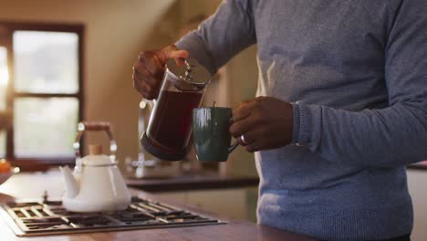 midsection of african american senior man in kitchen pouring coffee from pot