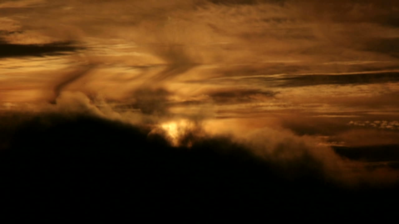 Wolken ziehen schnell über der orangefarbenen Sonne an einem sich verdunkelnden Himmel.