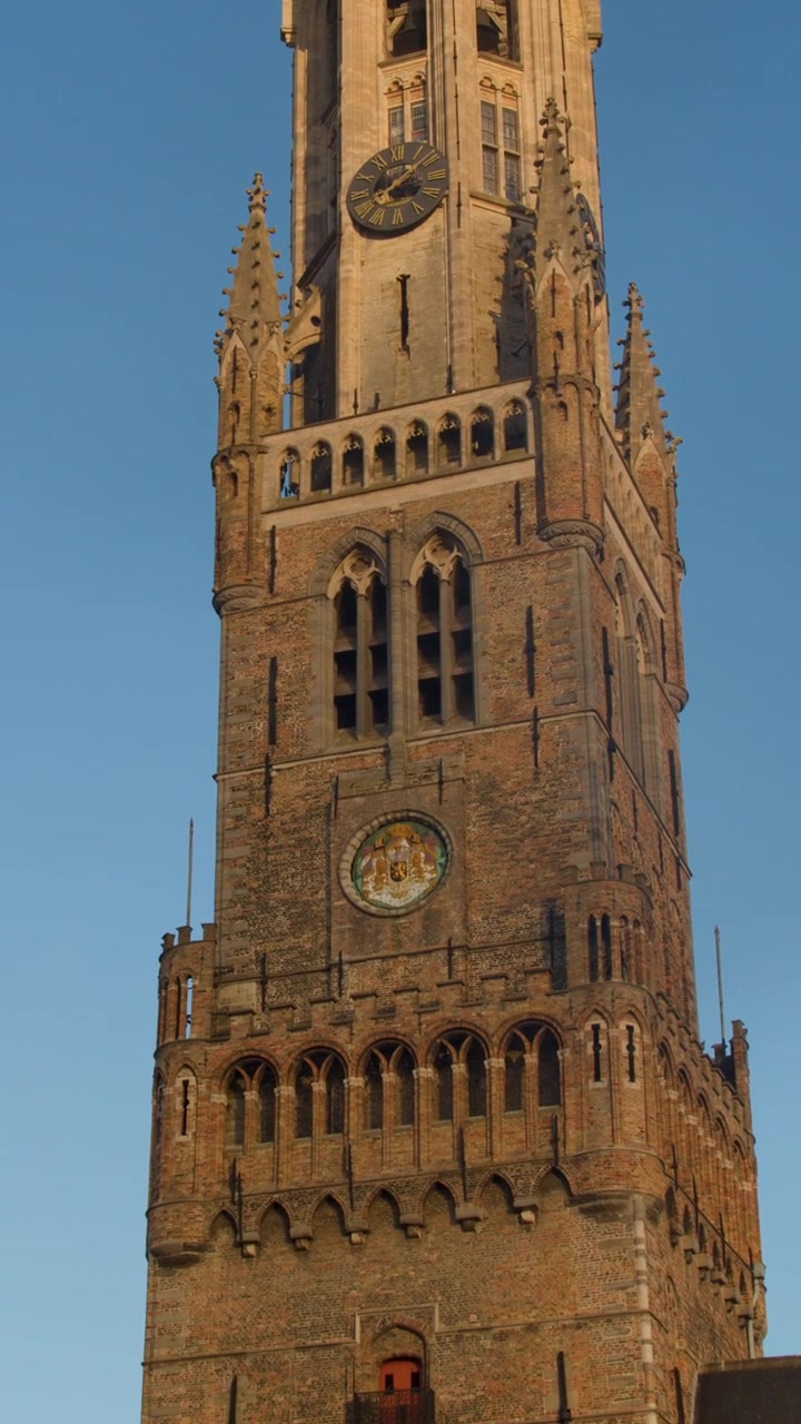Camera tilts upward along medieval brick clock tower, golden hour lighting, clear blue sky