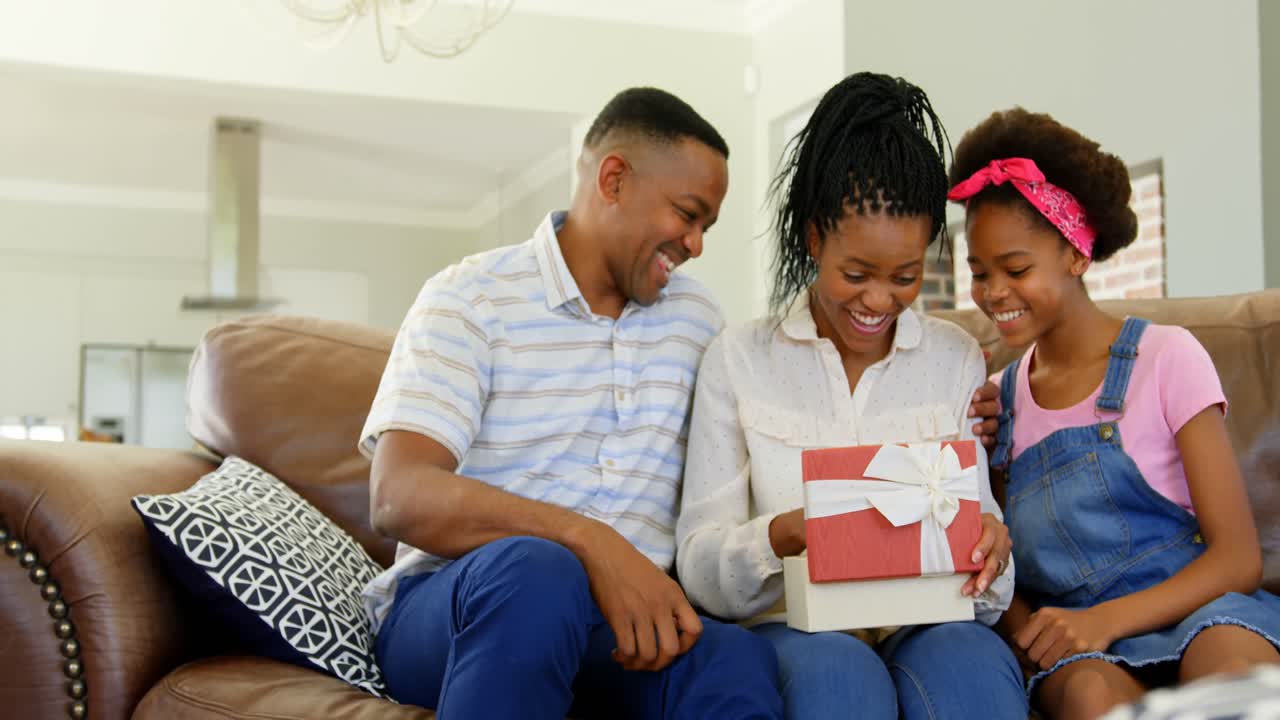 Front view of black father and daughter giving birthday gift to woman in living room at home 4k