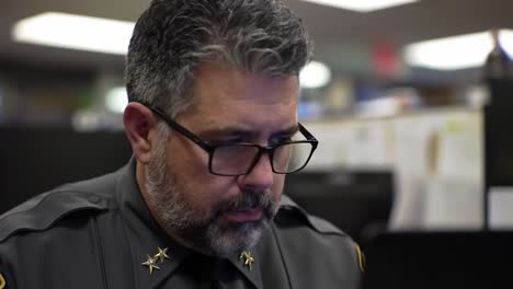focused law enforcement officer engaged in detailed work at desk amidst office environment, demonstrating dedication to duty and professionalism in critical situations