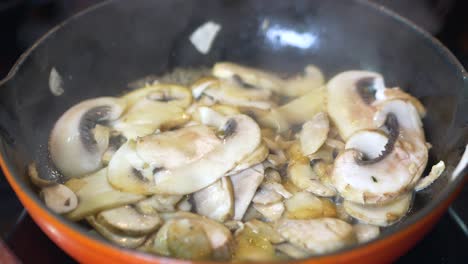 los champiñones en rodajas se fríen en una sartén roja caliente