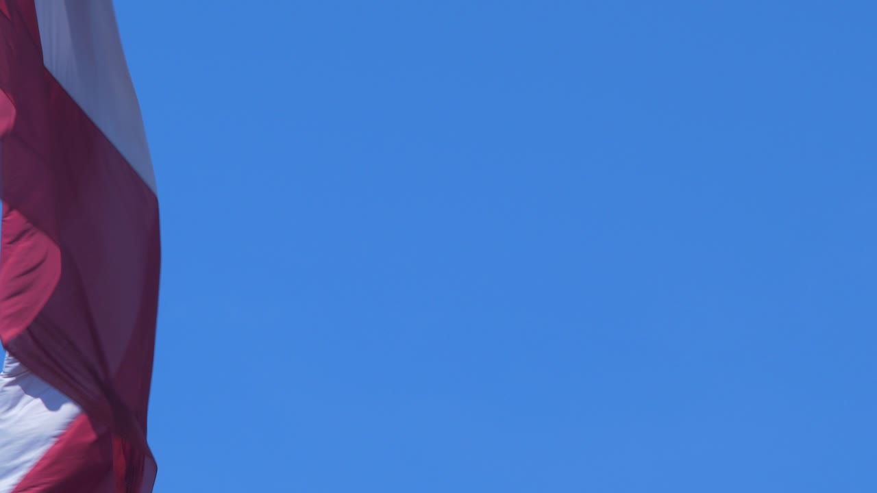 gran bandera letona ondeando lentamente en el cielo azul en un día soleado, primer plano