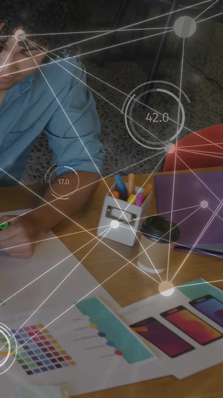 Vertical video: Designer using green pen, marking swatches for review as HUD nodes updating on desk