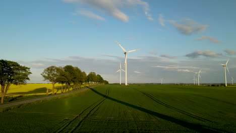 Rural-road-with-wind-turbines-spinning-creating-renewable-energy,-aerial