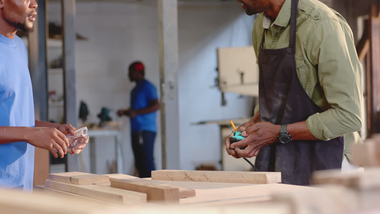 Measuring African American man wearing apron using tape measure on plank at workshop, copy space