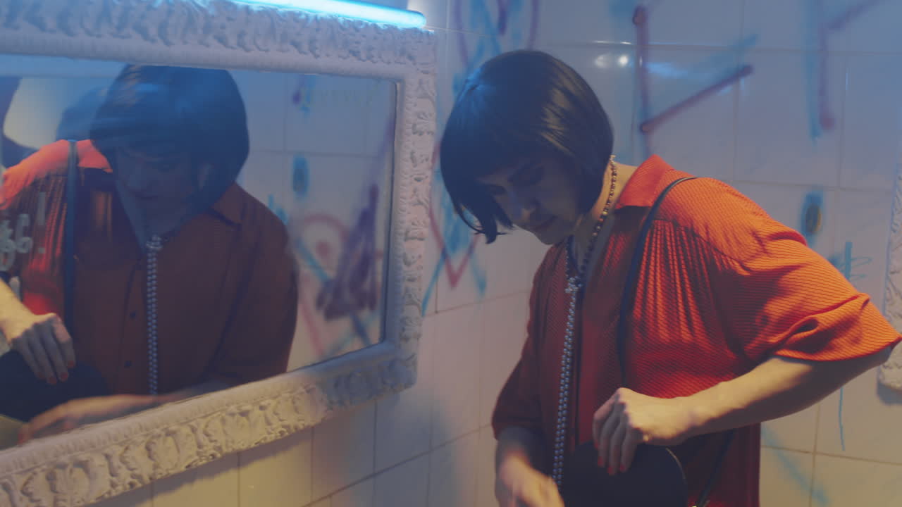 hombre transgénero arreglando maquillaje en el baño de un club nocturno