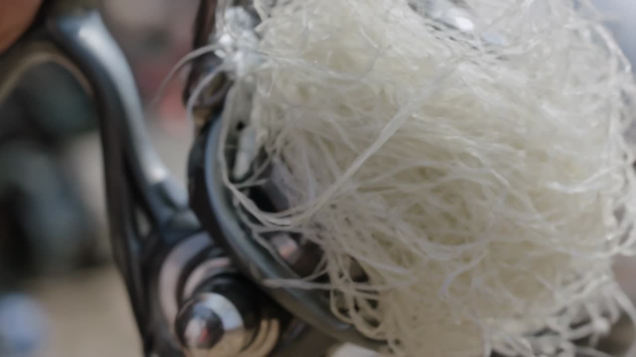 Finger rører ved metal og tråder hvid fiberkugle ind i klemmeringe på arbejdsbænk for at fastgøre komponent.