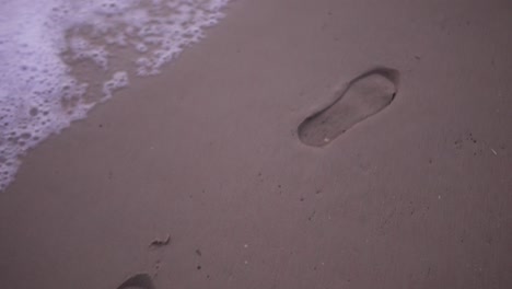 slow-motion tracking shot of foot prints on the beach with waves crashing