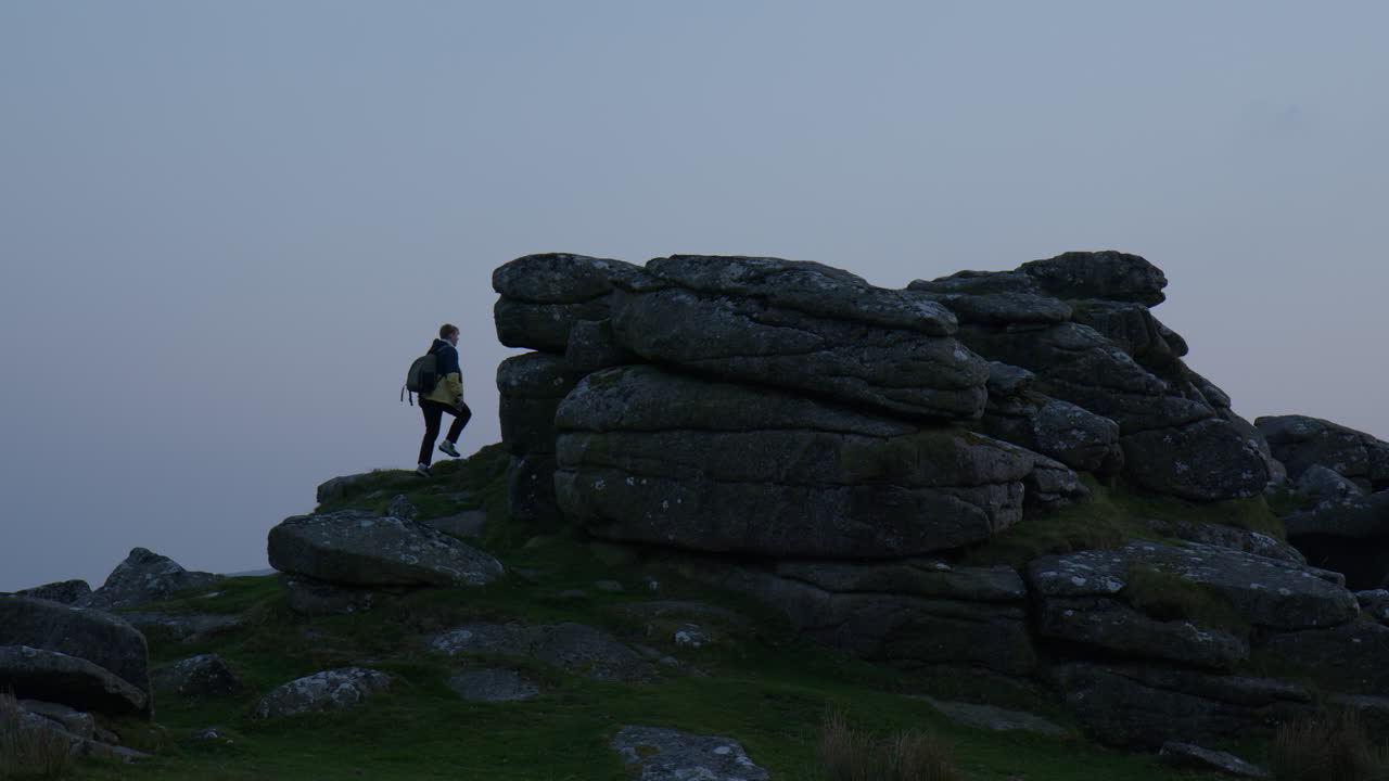 Backpacker Climbing On Scenic Tor At Sunset At Dartmoor National Park In Devon, UK. wide shot