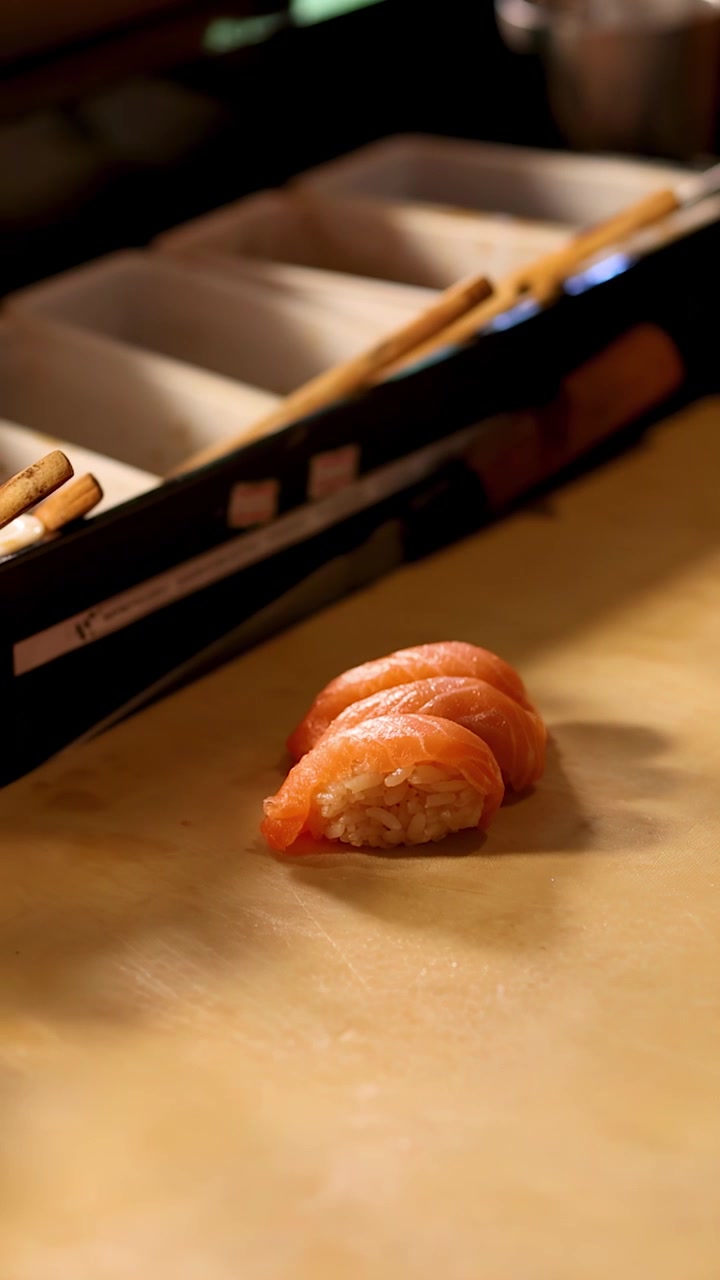 Statische Nahaufnahme von drei Stücken Lachs-Nigiri-Sushi auf einer professionellen Holztheke.