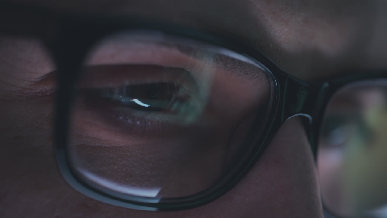 Closeup of person wearing glasses looking at computer screen at night