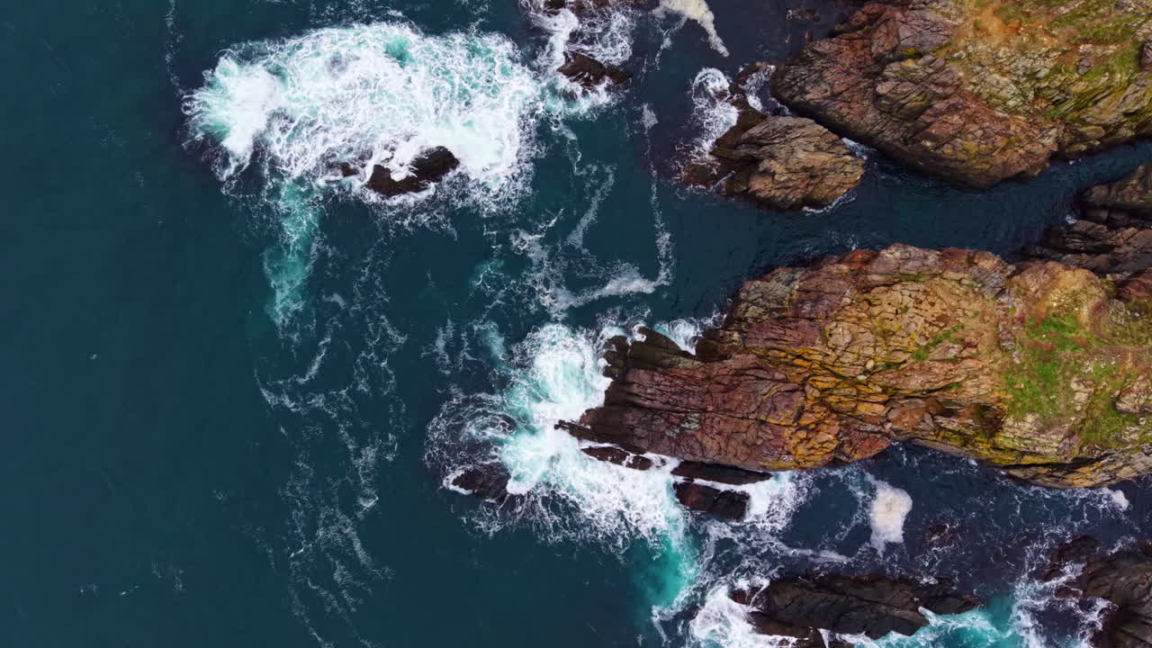 Le onde si infrangono sulle scogliere frastagliate, mentre i gabbiani sorvolano le acque scintillanti in una località costiera durante una giornata di sole