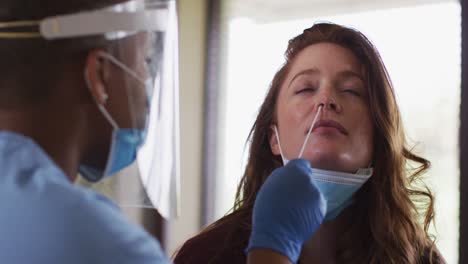 médica afroamericana que usa una máscara facial dando una prueba de cotonete de covid a una paciente
