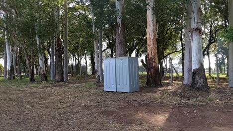 Viajar-Hacia-Adelante-Muestra-Un-Baño-Portátil-Público-Gris-Con-Un-Entorno-Natural-Tranquilo-En-Un-Bosque-En-Un-Día-Soleado,-La-Luz-Se-Filtra-En-La-Escena