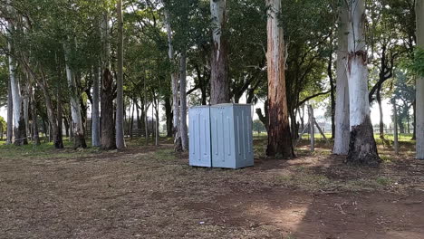 viajar hacia adelante muestra un baño portátil público gris con un entorno de bosque de naturaleza tranquila en un día soleado, la luz filtra la escena