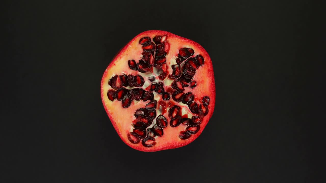 Siyah arka plan üzerinde dönen nar. Taze meyve suları, sebze, vitamin ve yaz konsepti. Yarım sulu narın üstten görünümü