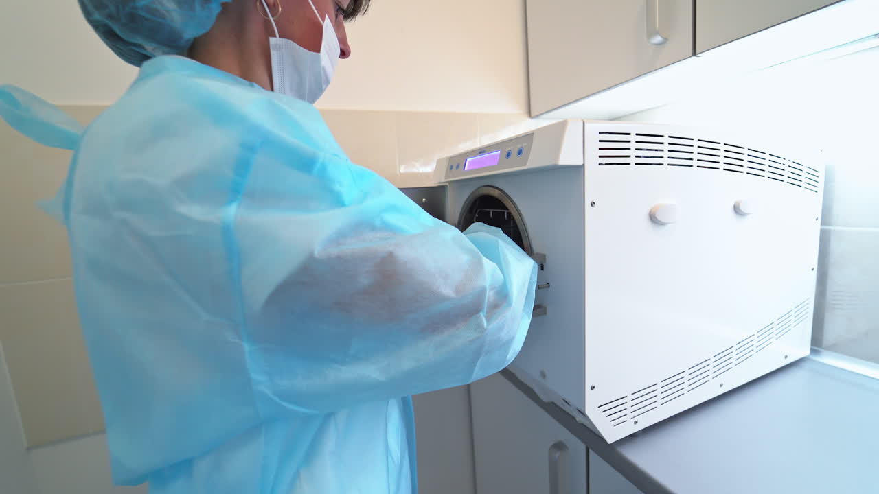 Female nurse takes sterile instruments out of sterilizer. Special equipment for preparation tools to various dental procedures.