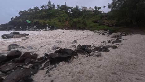 waves leaving foam on shore of snapper rocks during cyclone alfred in gold coast, queensland. panning shot