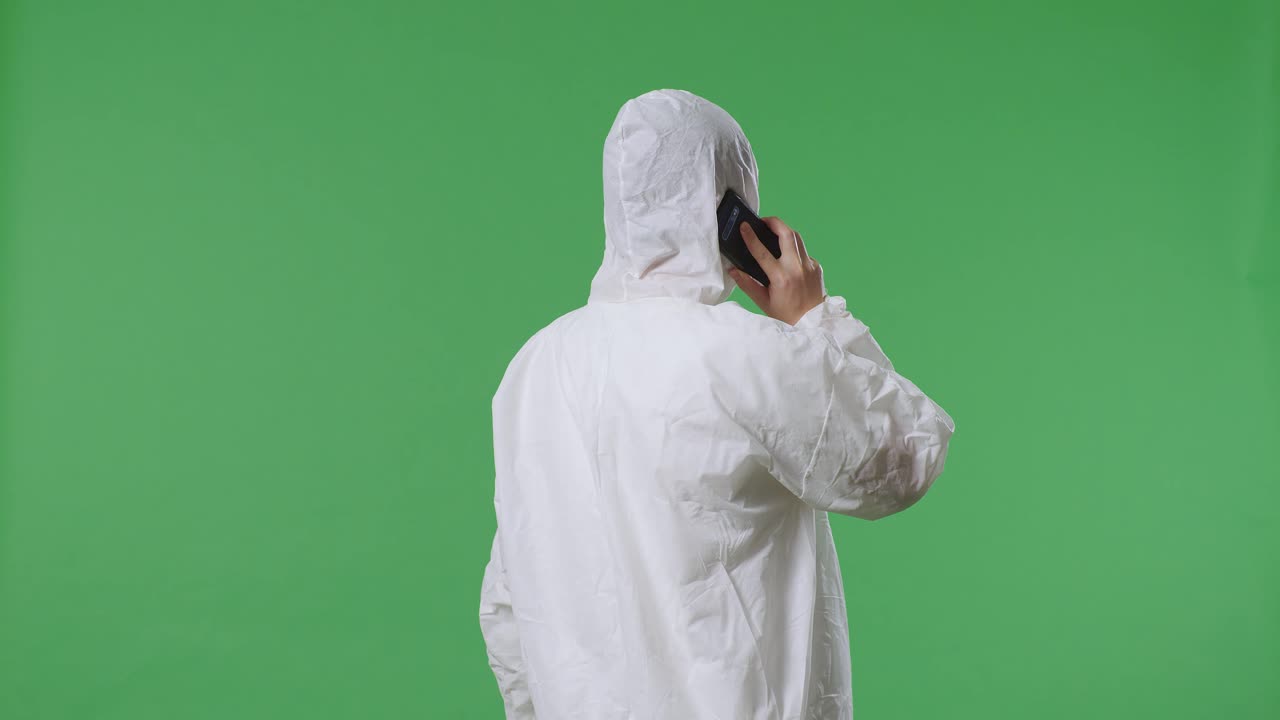 vista trasera de un científico masculino asiático hablando en un teléfono inteligente mientras está de pie en el fondo de la pantalla verde