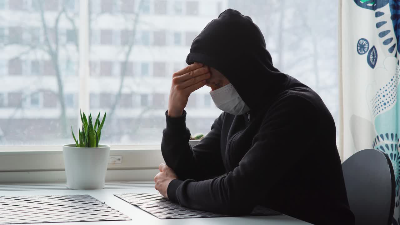 얼굴 마스크를 쓰고 테이블에 앉아 이마를 마사지하는 우울한 남자