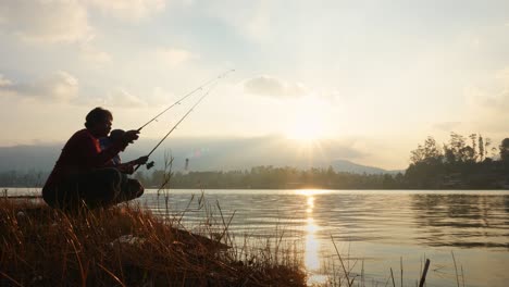 two men crouch on the lake shore throwing fishing rods into the lake