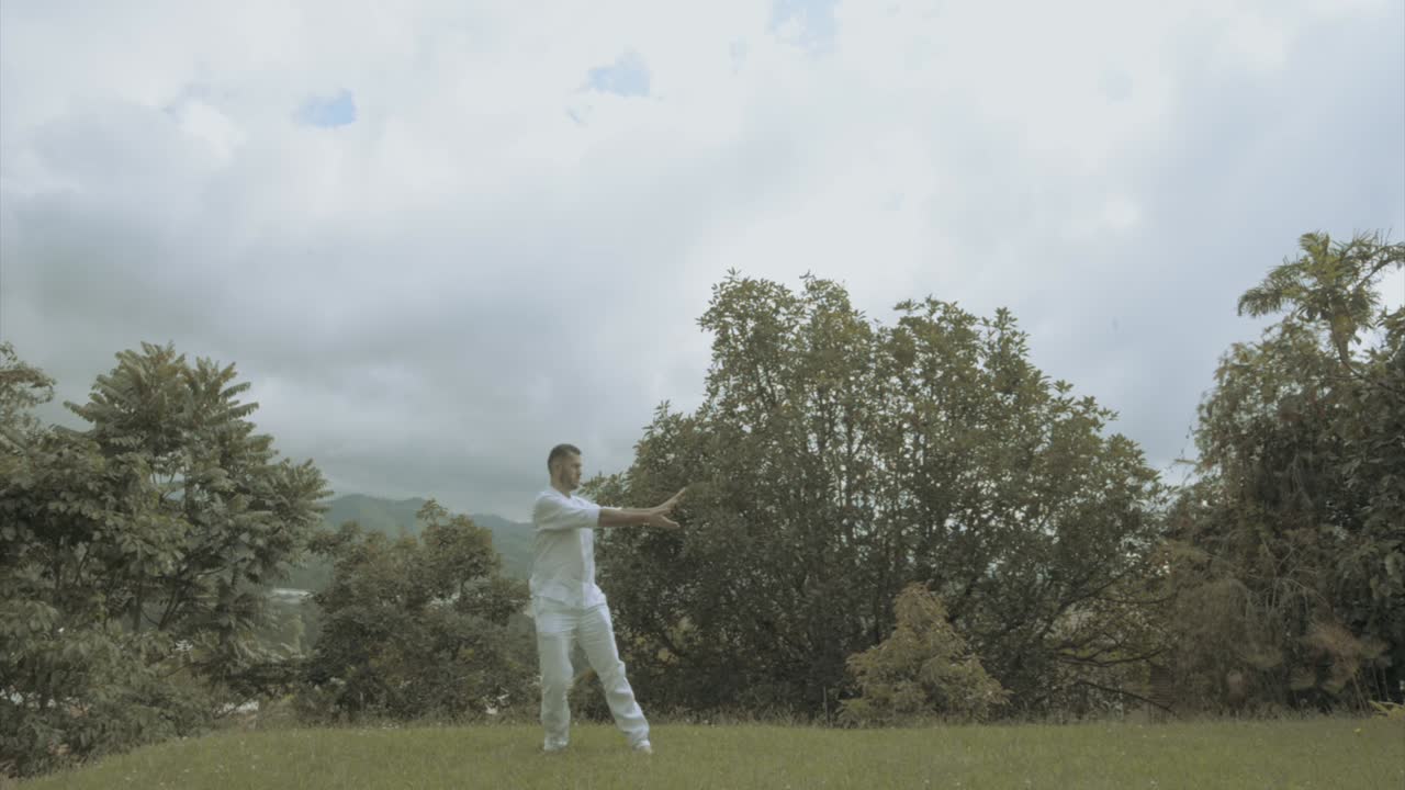 Young man in white Dress doing yoga meditation and spiritual movements in a beautiful green landscape mindfulness and tai chi