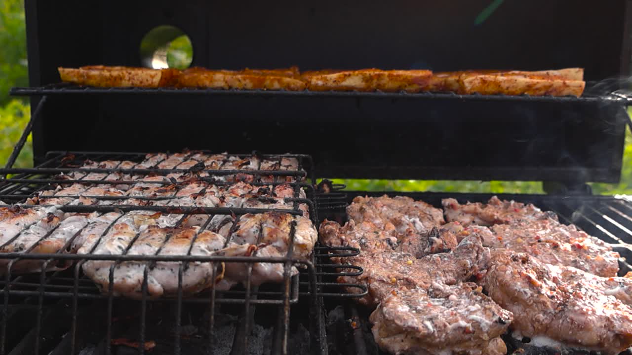 Close up view gliding over barbecue or barbeque meat and chiken pieces that are seasoned and cooking on a hot smoking grill outdoors during summer or autumn day, char marks are visible on the meat