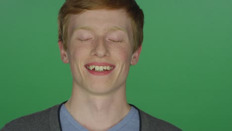 young man with red hair and freckles smiling, on a green screen studio background