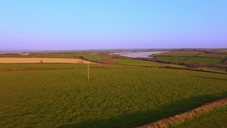 Aerial-drone-tracking-phoneline-mast-through-a-field-during-sunset