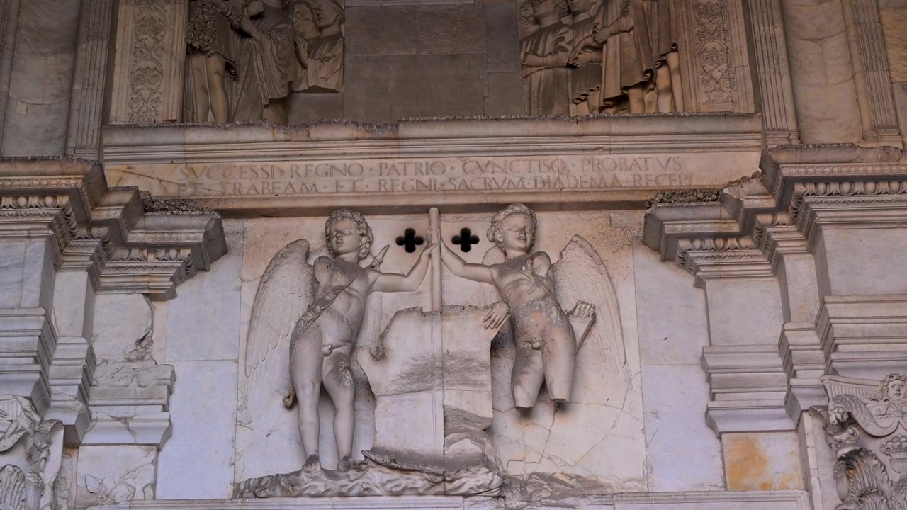 Putti alati scolpiti in marmo bianco reggono simboli araldici sull'ornata facciata del Castel Nuovo in un dettaglio architettonico ravvicinato