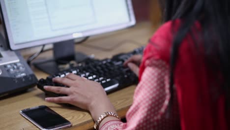 Lady-working-on-computer-in-the-office,-close-up-shot-over-the-shoulder,-Camera-paning-down