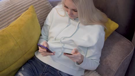 joven cliente femenina usando el teléfono móvil mientras está sentada en el sofá en casa.