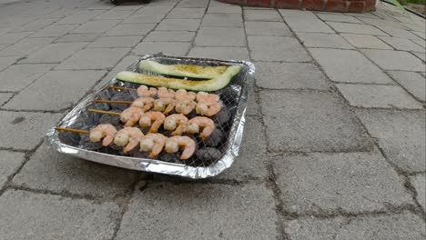 Locked-off-view-of-disposable-mini-BBQ-grill-with-Zucchini-and-Shrimp-skewers-SLOW-MOTION