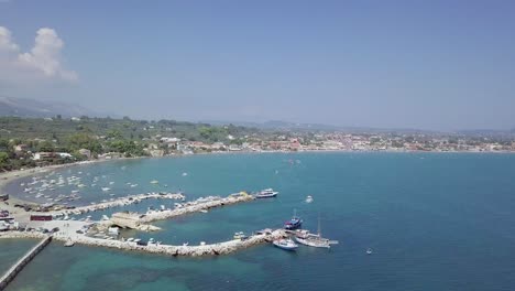 Schwenk-Drohnenaufnahmen-Der-Küste-Der-Insel-Zakynthos-In-Griechenland,-Mit-Blauem-Meer,-Einem-Kleinen-Hafen-Und-Ländlichen-Hügeln-Im-Hintergrund