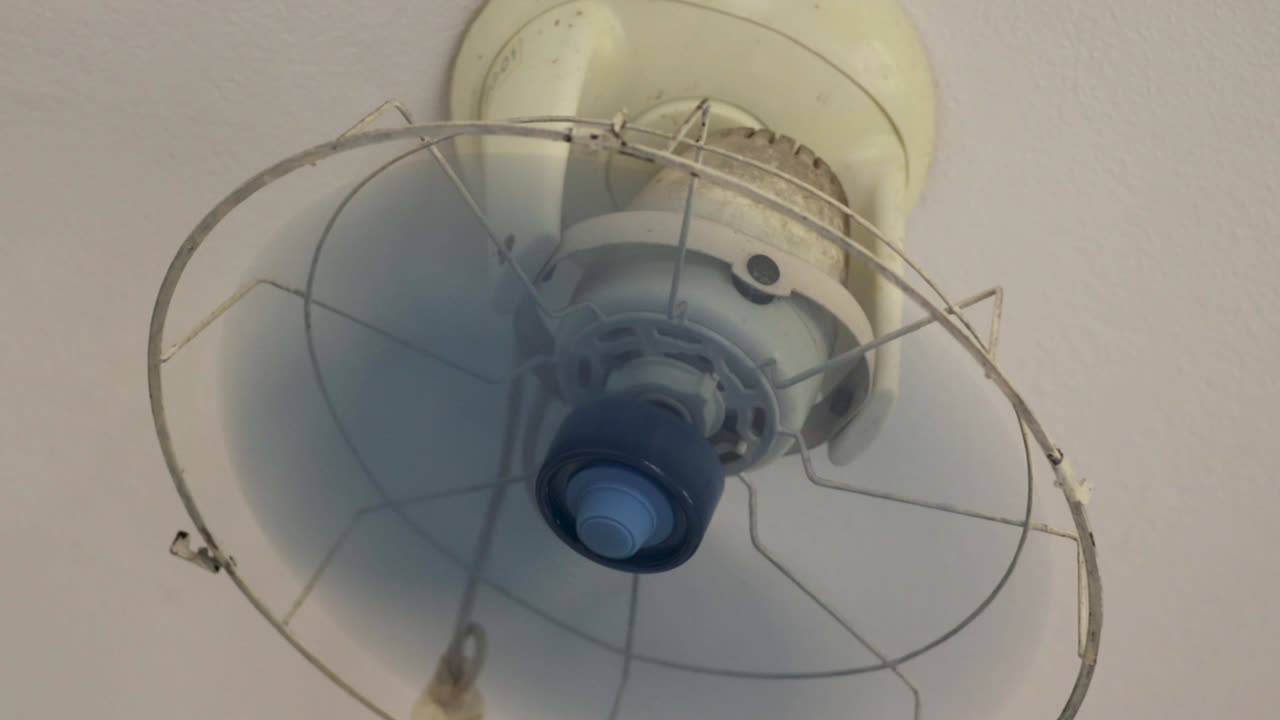 밝은 파란색 작은 먼지가있는 전기 천장 팬 시작 및 서서히 회전 낮은 지점에서 시야를 멈추십시오.