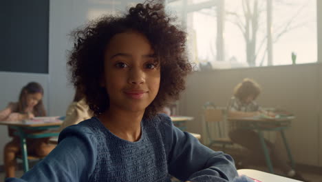 girl looking at camera in classroom. cheerful student sitting at desk at school