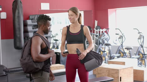 Un-Hombre-Afroamericano-En-Forma-Conversa-Con-Una-Joven-Caucásica-En-El-Gimnasio