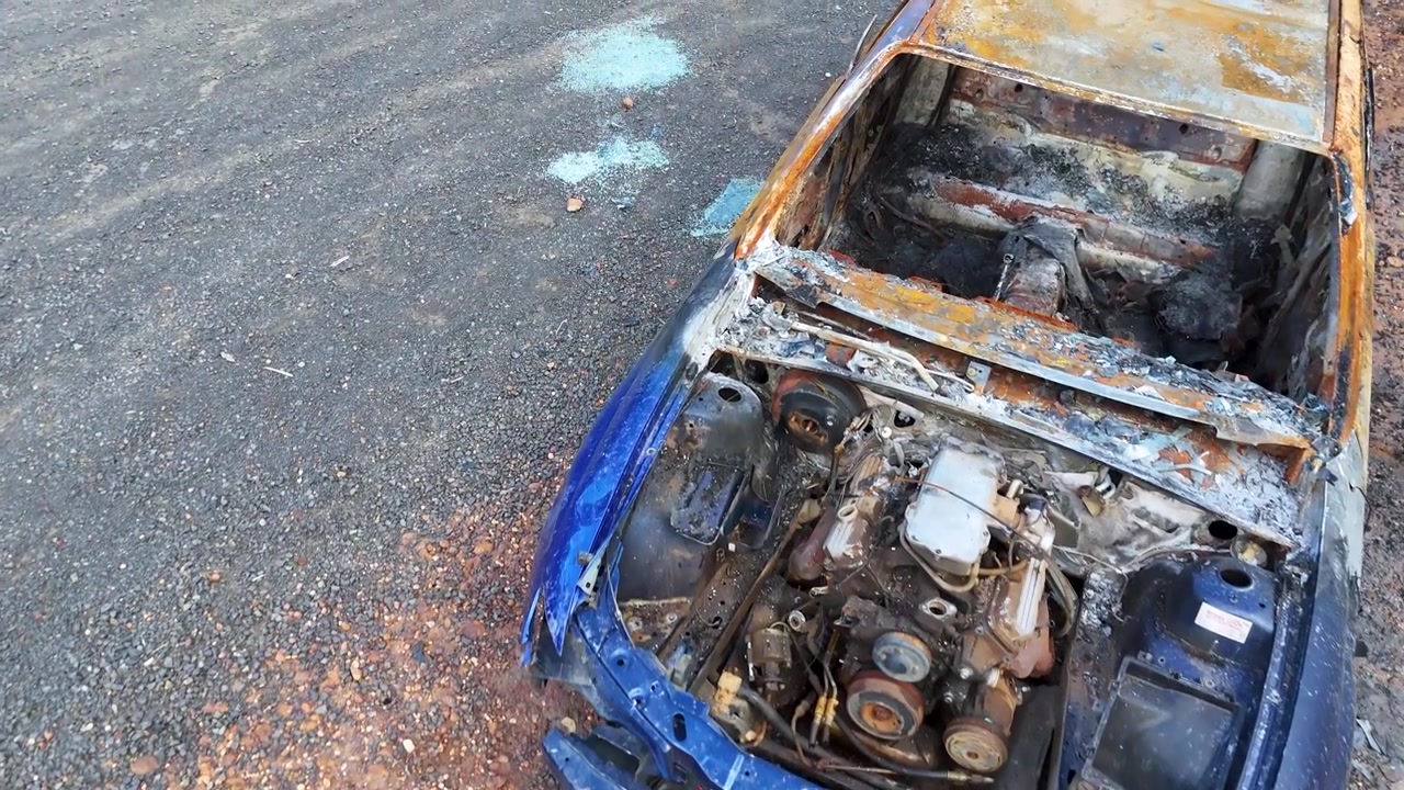 High angle tracking shot of a charred vehicle frame and engine bay in Australia.
