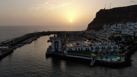 Puerto-De-Mogan:-Vista-Aérea-Con-Movimiento-De-Alejamiento-Y-Durante-La-Puesta-De-Sol-De-La-Ciudad-De-Puerto-De-Mogan-Con-Hermosos-Colores