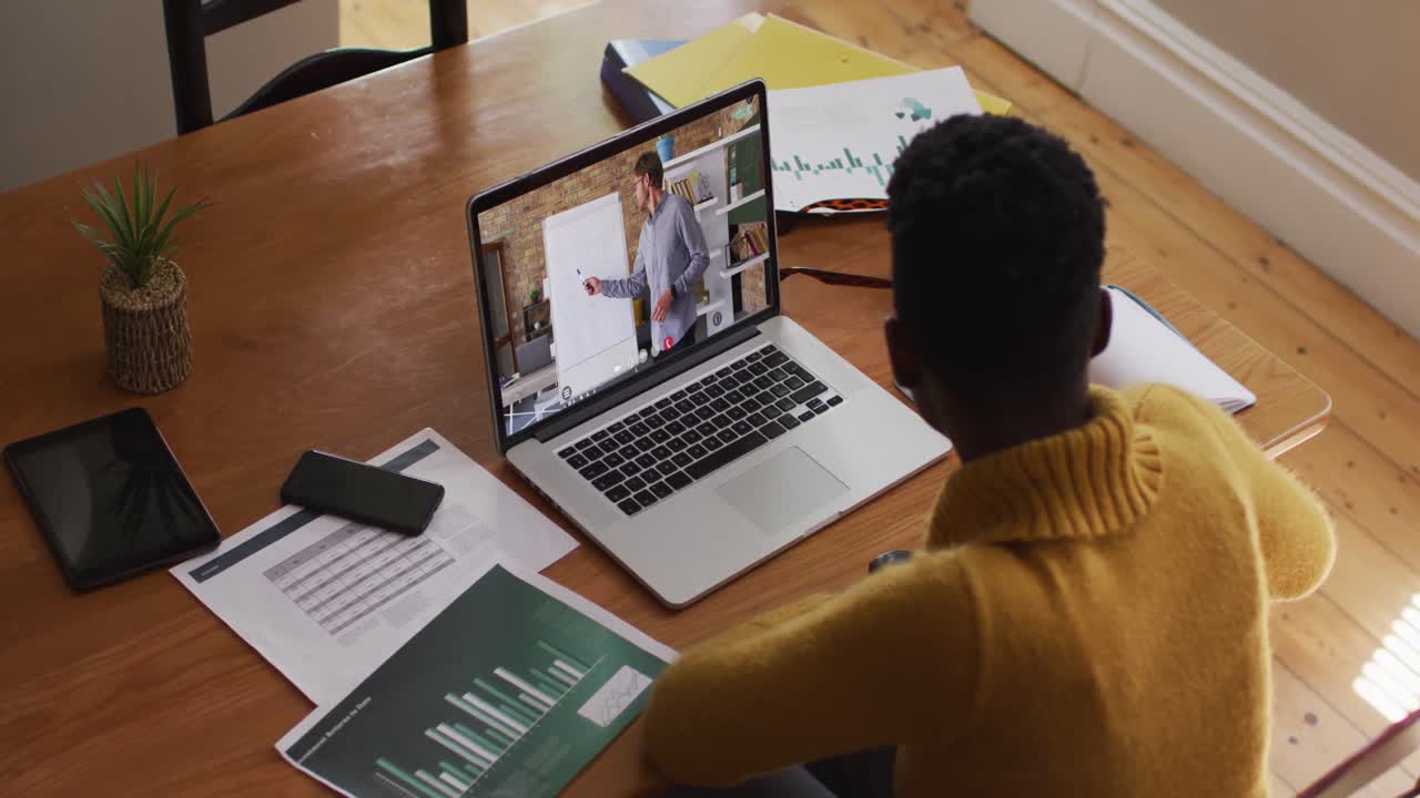 estudiante afroamericana usando una computadora portátil en una videollamada con un profesor masculino
