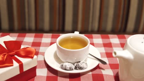 homemade surprise dinner for an important event: birthday, anniversary, valentine's day. a simple meal on a date, a gift in a red and white box with a bow on the table near a delicious pizza and a cup of herbal tea with a teapot