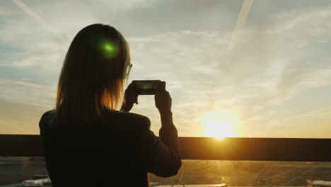 ビジネス スーツを着た女性が夕日の写真を撮る