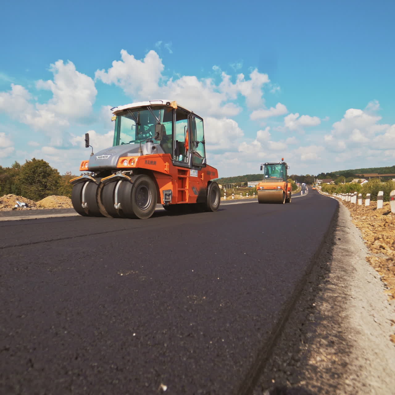 Process of pressing fresh asphalt on the road in a bright sunny day. Two new compactors working on the new road leveling up hot bitumen in summer.