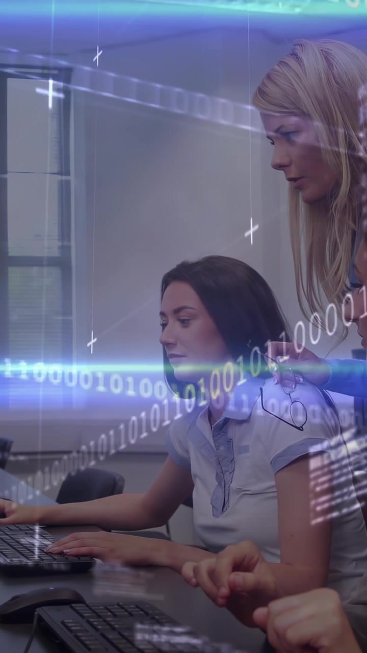 Video verticale: Mentore che si china per guidare il tirocinante che digita codice binario, con PC in sovrimpressione, assistendo la formazione in laboratorio.