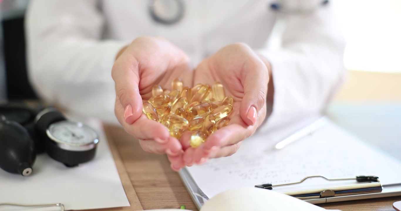 Una persona in camice bianco tiene tra le mani una manciata di capsule dorate.
