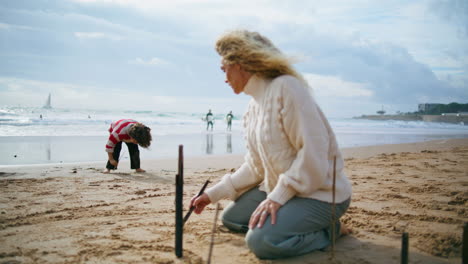 Familia-Escribiendo-Arena-De-Playa-Juntos.-Madre-Creativa-Hijo-Descansando-En-La-Orilla-Del-Océano